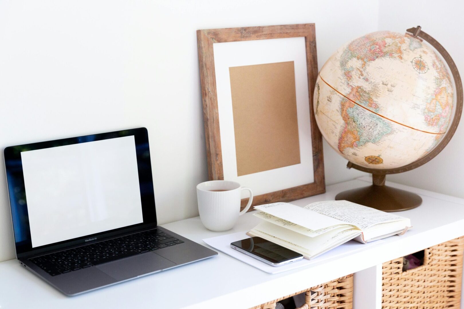 A laptop and cup on a desk with a globe.